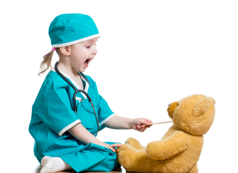 Niña vestida de médico jugando con oso de juguete