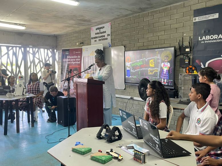 mujer, ministra de educación, habla a estudiantes jóvenes de colegio en aula con computadores 