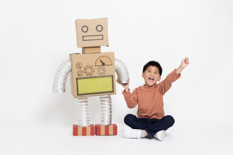 Niño sentado tomado de la mano de robot  de juguete con cara y cuerpo de cartón