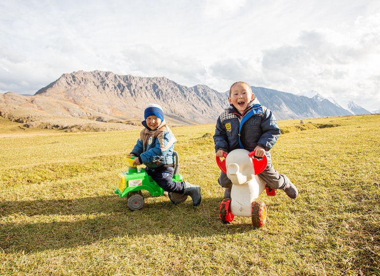 dos niños en el campo montando en carritos de plástico y riendo