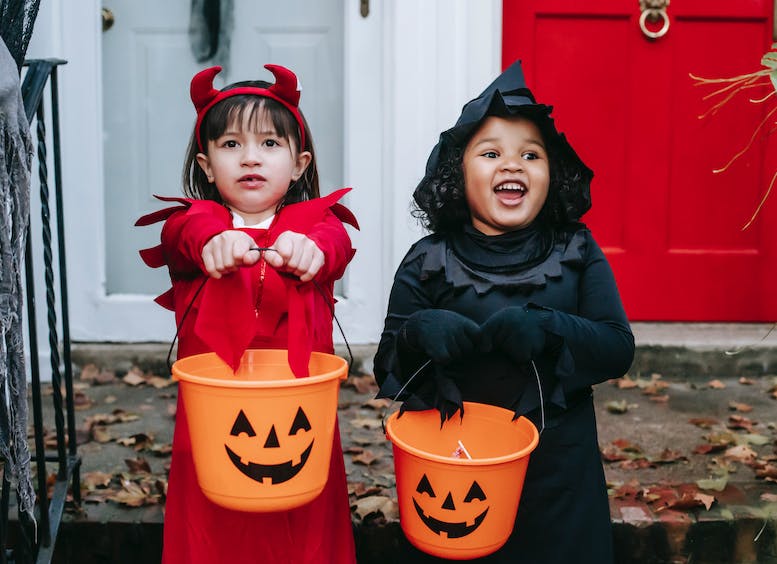 Dos niñas disfrazadas sonriendo, sostienen baldes color naranja, pidiendo dulces