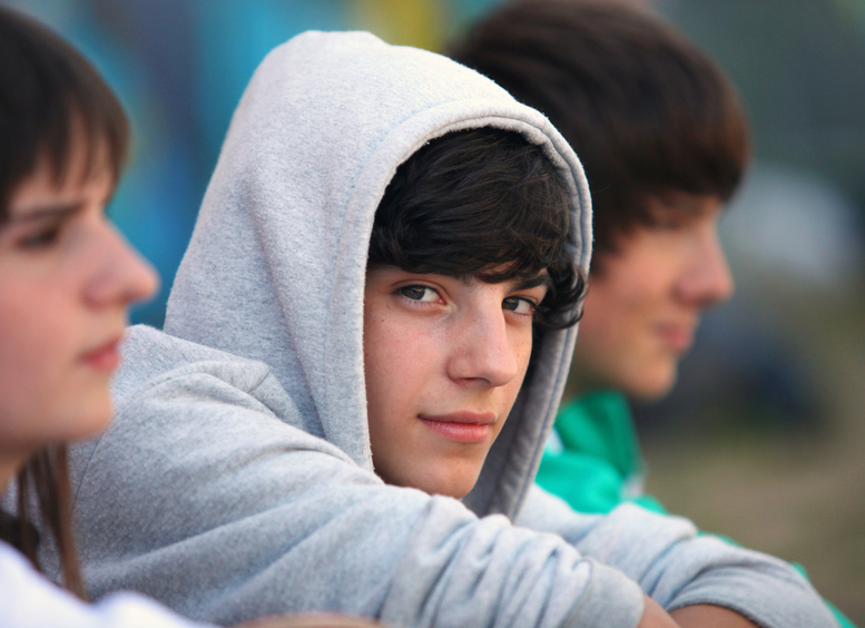 Tres adolescentes sentados, uno mirando a la cámara con chaqueta gris de capota