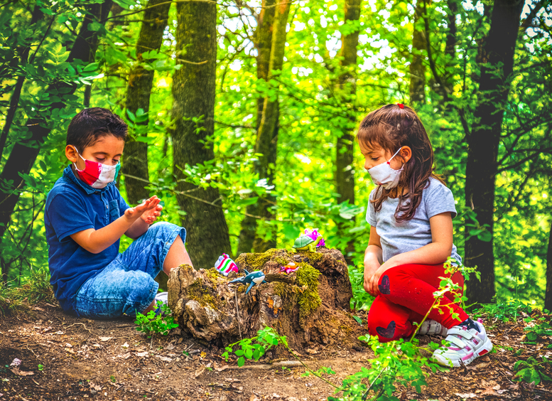Una niña y un niño con tapabocas, jugando en el bosque