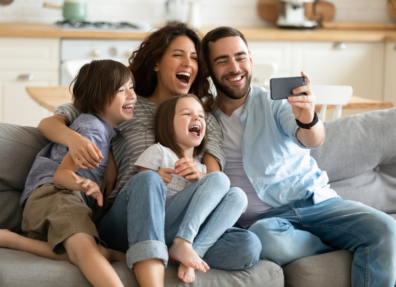 padres felices con niños pequeños usando un smartphone juntos sentados en el sofá en casa.