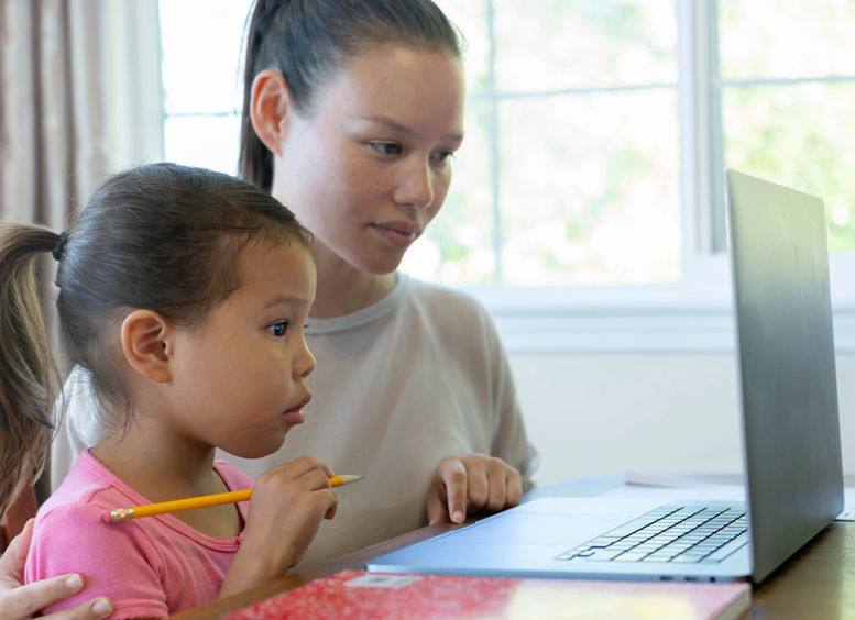Madre e hija en frente de un portátil, y la niña sostiene un lápiz muy atenta a la pantalla