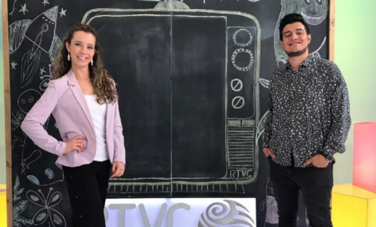 Una mujer y un hombre jovenes, de pie frente a un tablero que tiene pintado con tiza un televisor