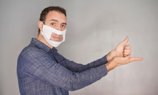 Foto de hombre con una mascarilla de sordomudo, mostrando el gesto de ayuda en lengua de señas