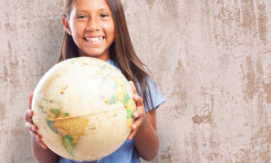 Adolescente mujer sonriendo mientras sostiene un globo terráqueo que muestra a América Latina y el Caribe