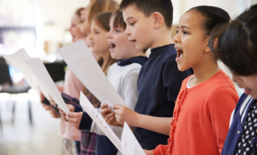 Grupo de niños y niñas cantando en un coro. Sostienen un papel en la mano
