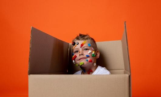 Niño escondida entre una caja de cartón, sonriente, con varias pegatinas en la cara