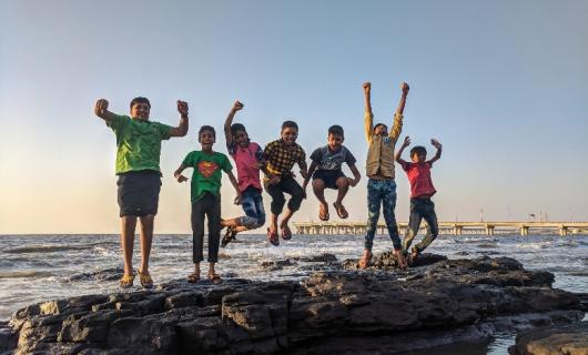 siete niños saltando sobre un tronco a la orilla del mar