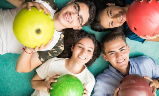 Foto de adolescentes multiétnicos mostrando bolas de colores, acostados en el piso y sonriendo