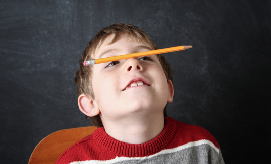Niño en clase distraido sosteniendo un lápiz sobre la nariz