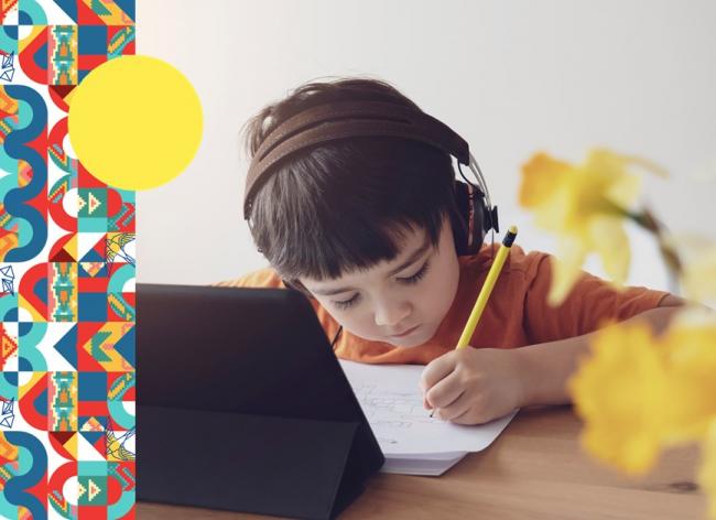 Foto de un niño estudiando sobre un escritorio con computador, hojas y papel