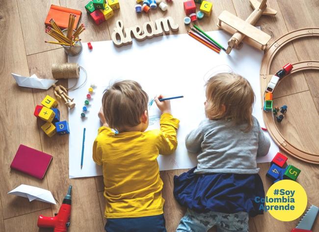 Foto de niño y niña pequeños escribiendo con lápices de colores sobre una cartelera