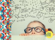 Foto de una niña con gafas entre una mesa mirando hacia arriba unas fórmulas matemáticas