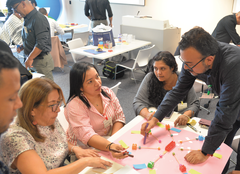El Ministerio de Educación avanza en la consolidación de la Red Nacional de Docentes de Formación Integral con la comunidad de aprendizaje en Ciencia, Tecnología e Innovación Varios docentes, hombres y mujeres sentados trabajando alrededor de una mesa y un hombre les da indicaciones