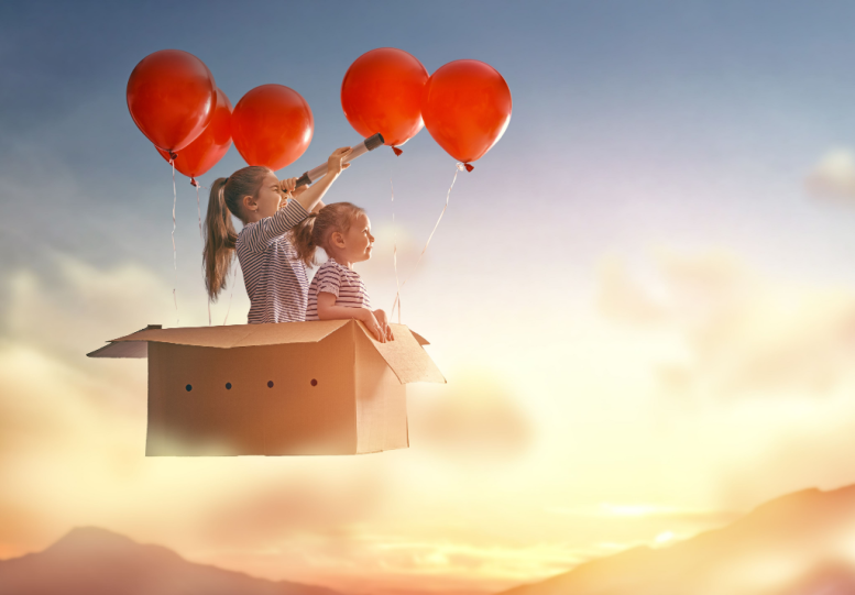 Dos niñas vuelan en caja de cartón con globos de aire rojos.