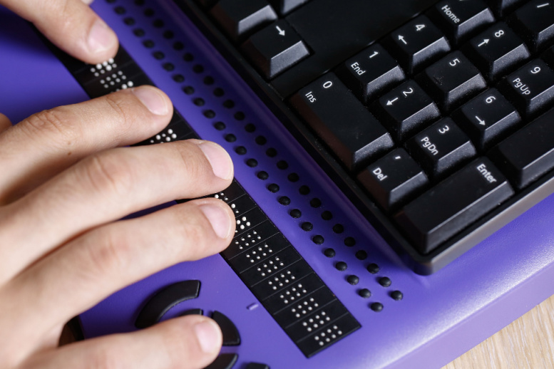 Manos de persona que usa teclado braille para computador. Ayuda para la ceguera, disfunción visual