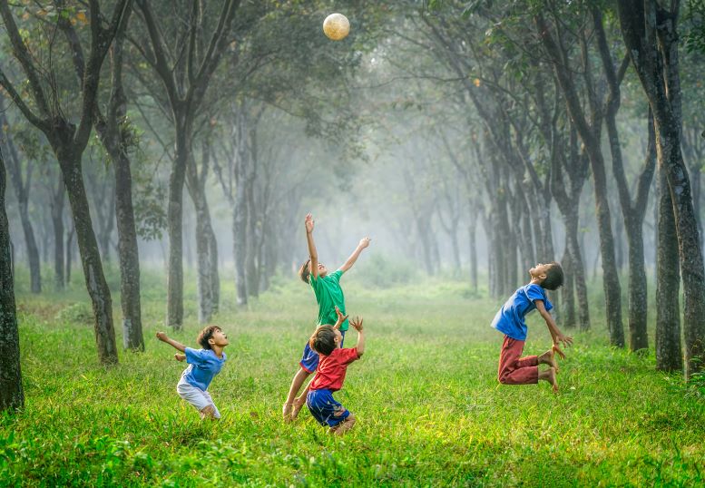 Cuatro niños en un campo soleado, brincan para atrapar un balón