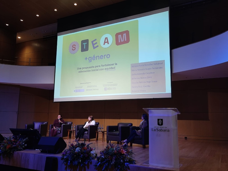 Foto del auditorio con los panelistas y una pantalla en el fondo con el título STEAM más género
